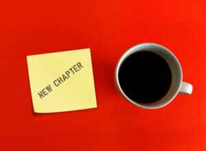 Red background with a cup of coffee and a post-it note that says, "New chapter" to indicate reinventing yourself in a new veterinary career