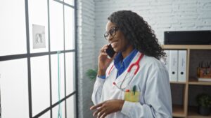 Black female veterinarian in a white coat smiling and talking on a cell phone