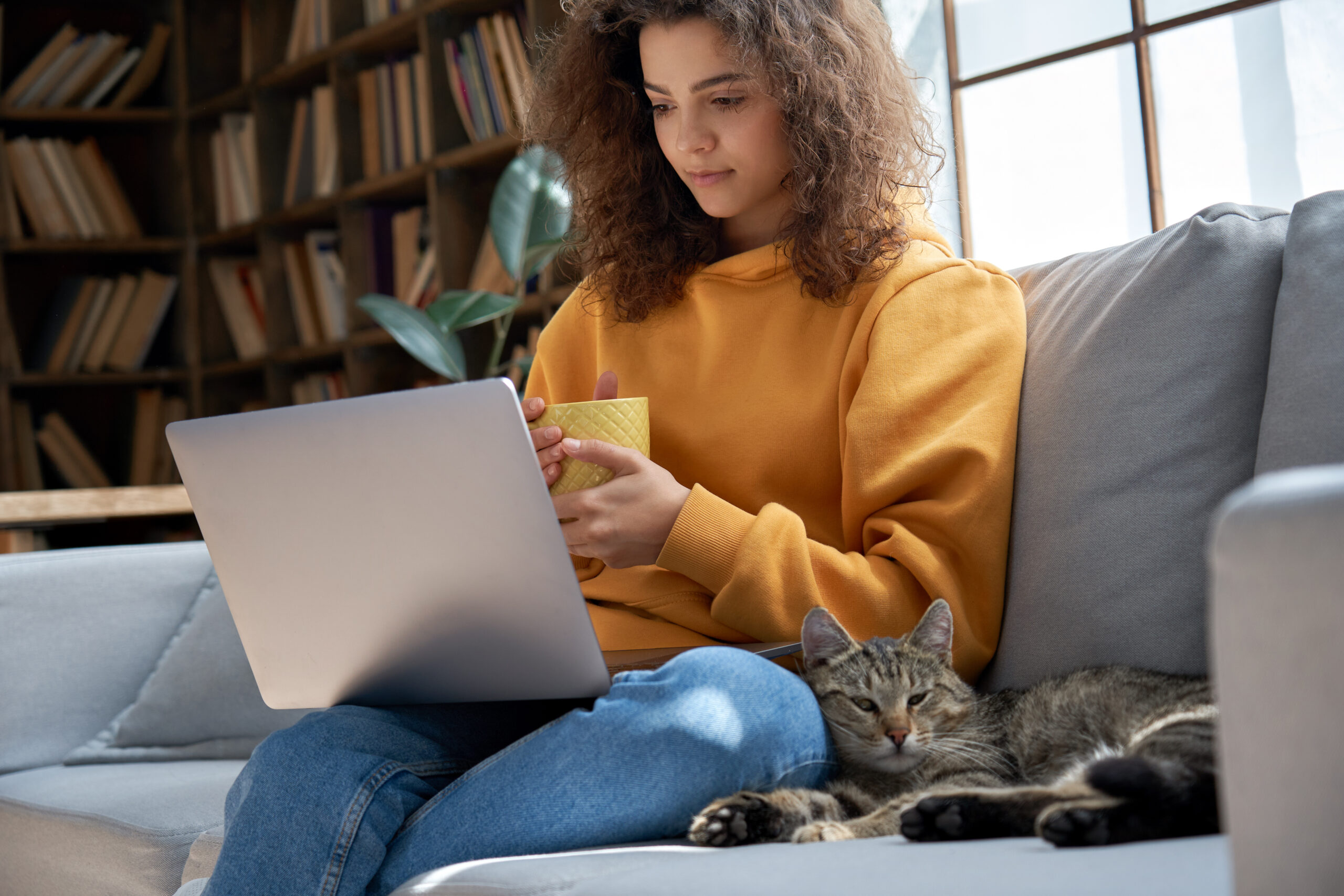 Young woman sitting on a couch with a cat reading a veterinary practice newsletter on a laptop