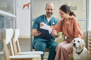 Male veterinarian reviewing test results with female owner, while a large white dog sits by her side
