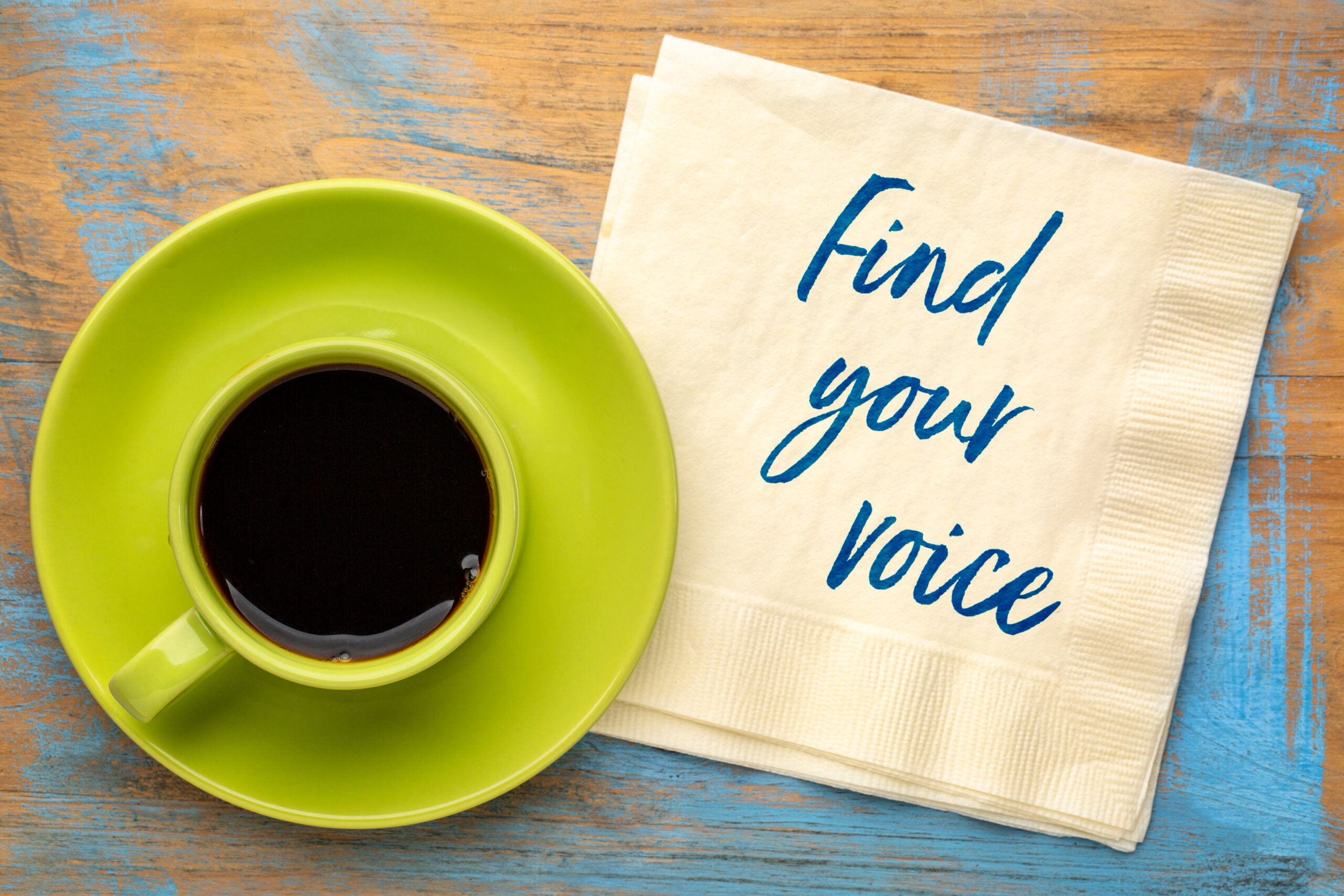 Cur of coffee on table beside napkin with writing that says "Find your voice."