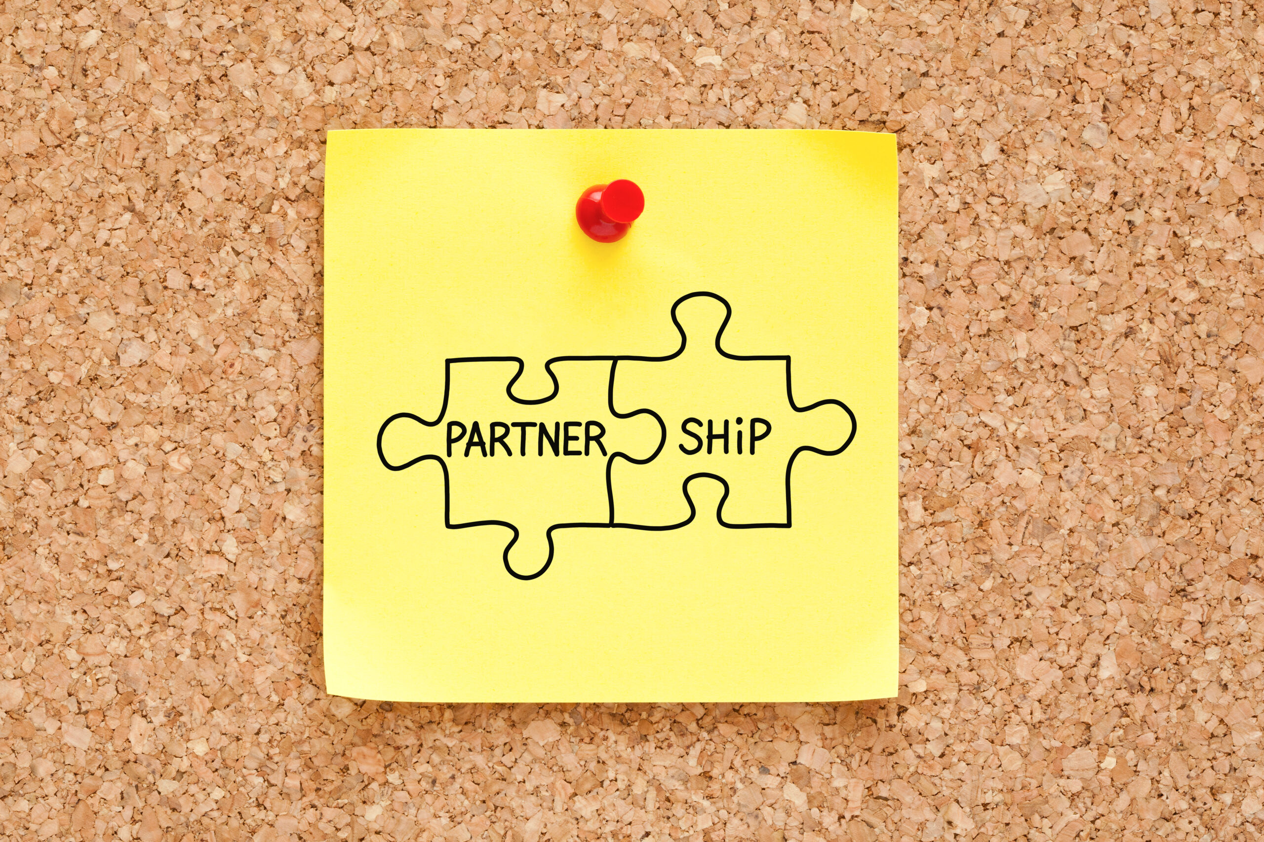 Sticky note showing two interlocking puzzle pieces with "partner" and "ship" written on them, signifying the partnership between a business and a professional copywriter